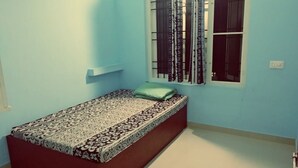 A single bed with a patterned bedspread, a green pillow, and a window with decorative curtains. - Noise free home stay (Eranakulam)