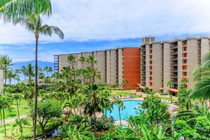 A hotel with multiple floors, a swimming pool, and lush greenery.