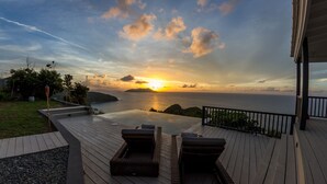 A wooden deck with two wicker lounge chairs facing a sunset over the ocean. - Stylish, Secluded Villa with Pool, Hot tub and Stunning Views (Mount Healthy)