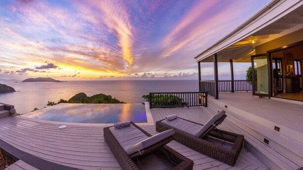 A deck with lounge chairs and a view of the ocean at sunset. - Stylish, Secluded Villa with Pool, Hot tub and Stunning Views (Mount Healthy)
