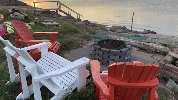Outdoor seating with Adirondack chairs and a fire pit by a waterfront.