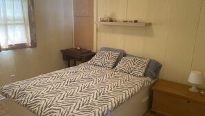 A single bed with a zebra-patterned bedspread, a bedside table with a lamp, a shelf with decorative items, and a window with curtains.
