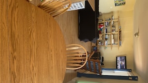 A dining area with a round wooden table and chairs, a black sofa, and a bookshelf against the wall.
