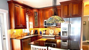 A kitchen with wooden cabinets, a stainless steel refrigerator, a microwave, and a dining area with a white chair.