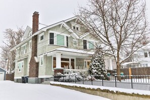 Een huis met twee verdiepingen, een veranda, een schoorsteen en een met sneeuw bedekte tuin.