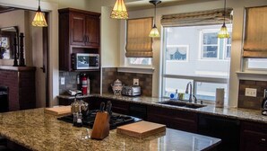 Una cocina con encimeras de granito, armarios de madera, microondas integrado y una isla grande con estufa.