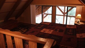 A cozy attic bedroom with a large window, a wooden bed, and a lamp on a nightstand. - Privacy & Location! One acre & 2min from town. Central AC. Covered patio. (Ruidoso)