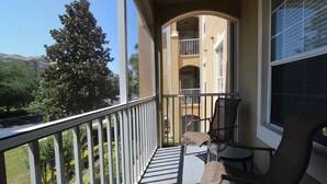 A balcony with two chairs and a small table, overlooking a garden and a building with balconies.