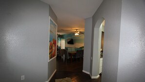 A hallway with a dining area in the background, a ceiling fan, and a painting on the wall.