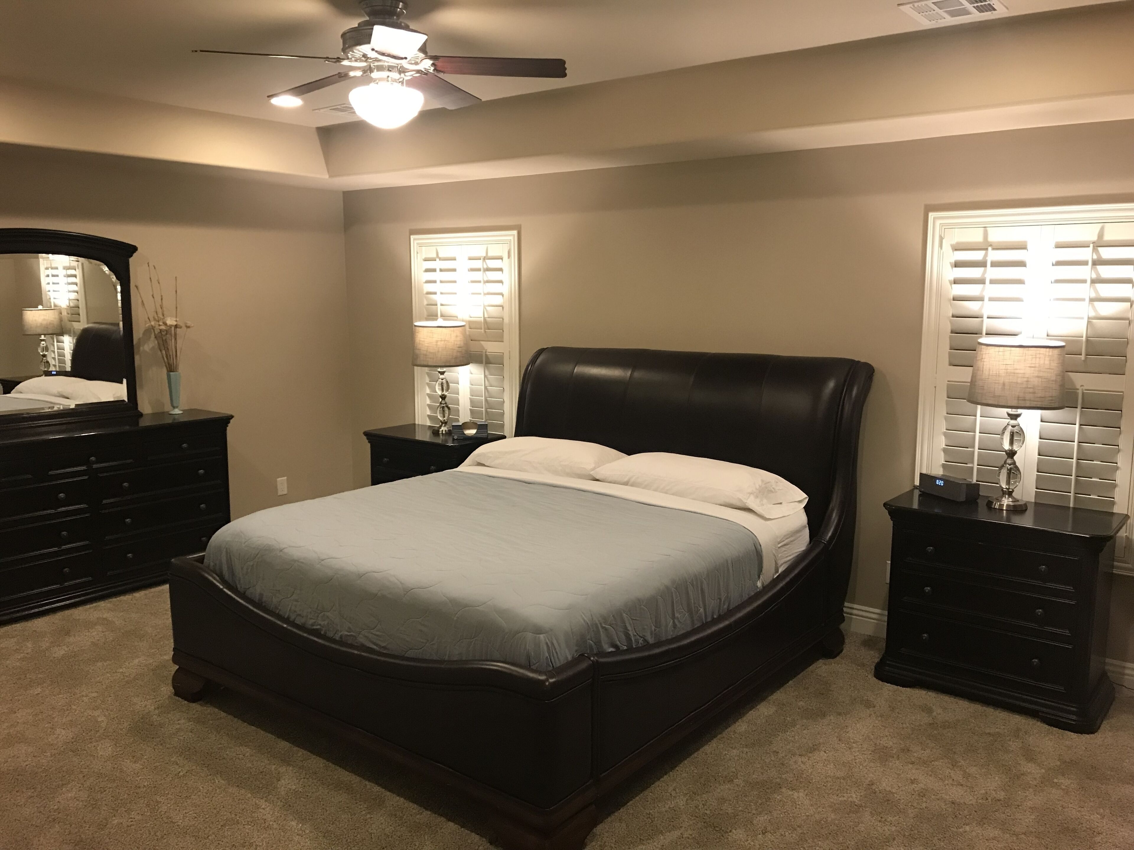 A bedroom with a bed, two nightstands, a dresser, a ceiling fan, and a window with blinds.