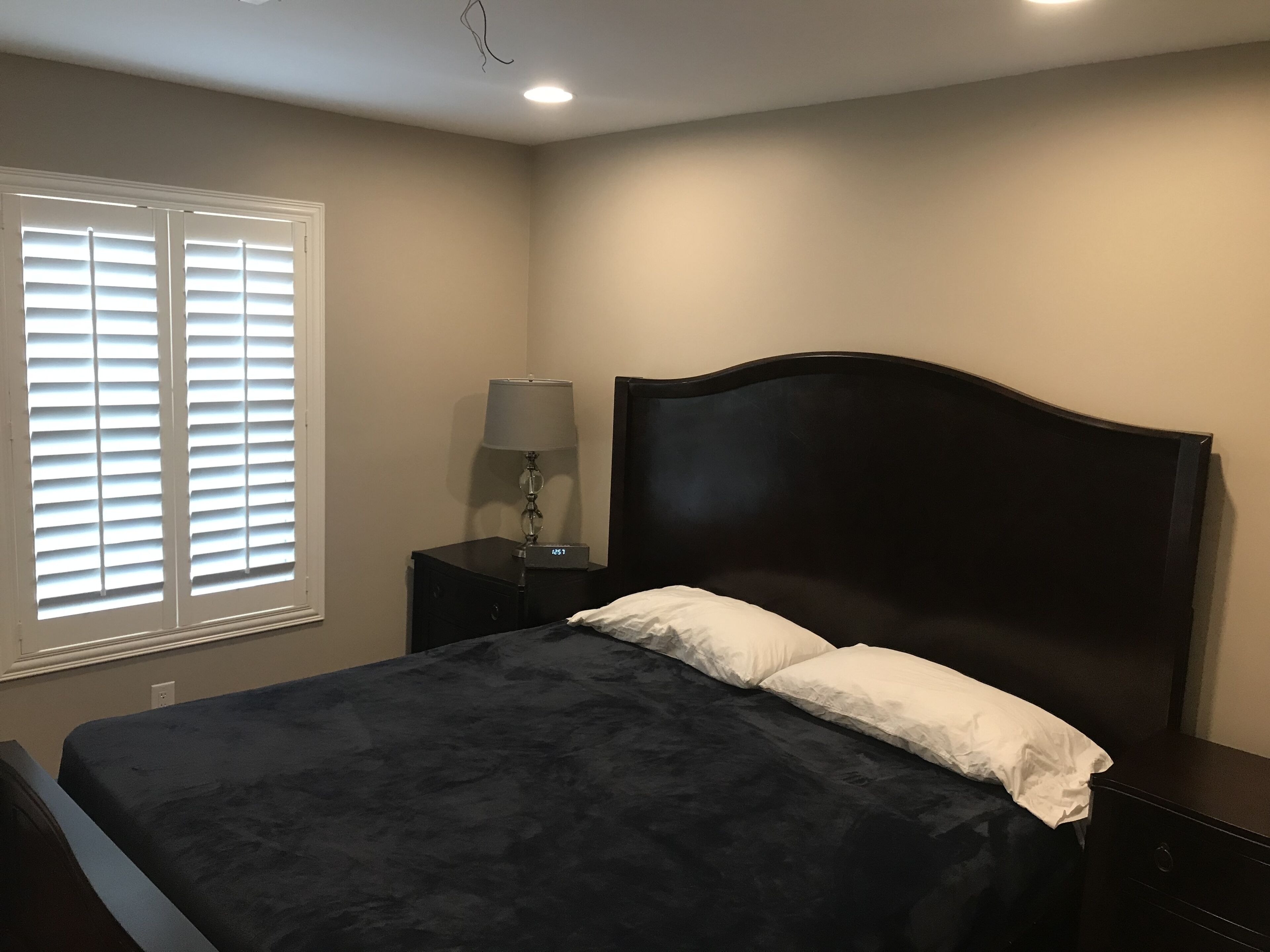Quarto com cama, mesa de cabeceira, abajur e janela com persianas.