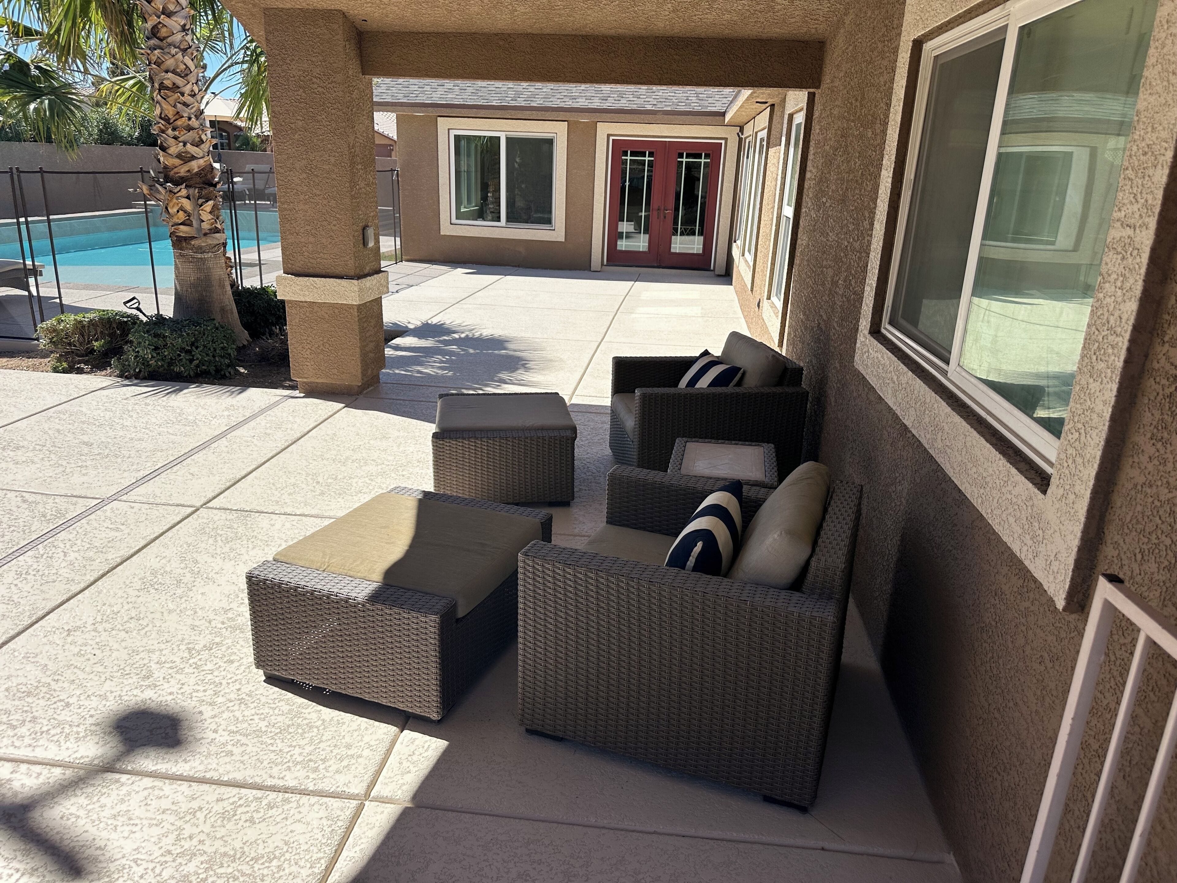 Un'area patio esterna con mobili in vimini, una piscina e un edificio con una porta rossa.