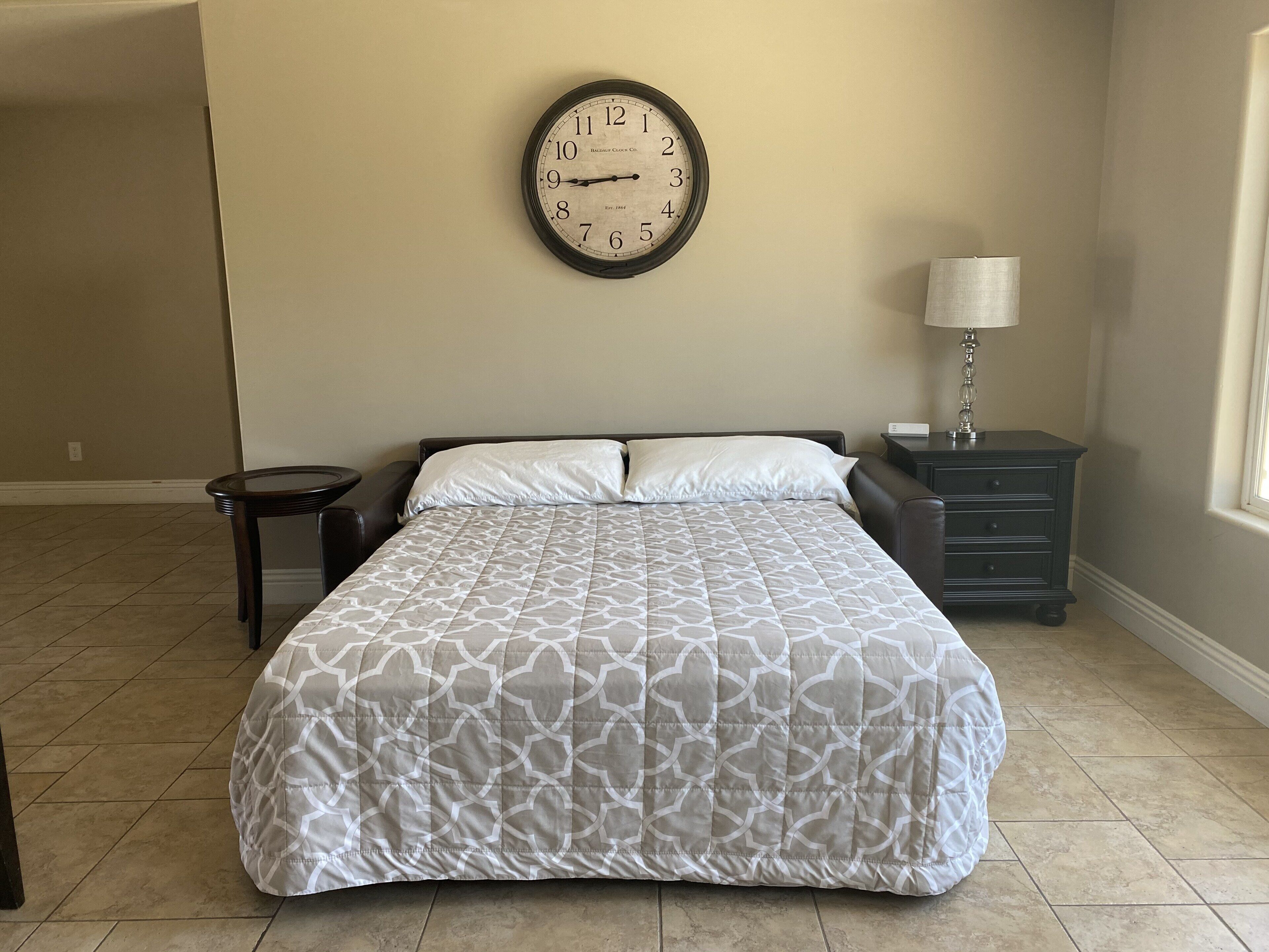 Un dormitorio con cama, un reloj, una mesita de noche y una lámpara.