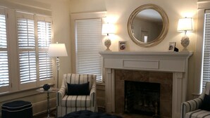 A living room with a fireplace, striped armchairs, a tufted ottoman, and a patterned rug.