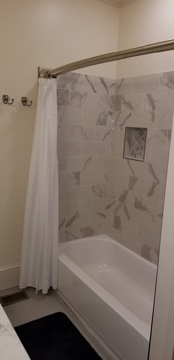 A bathroom with a bathtub, a shower curtain, and marble-patterned tiles.