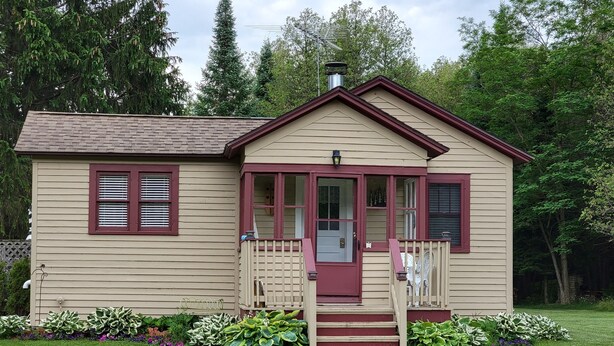 Ein zweistöckiges Haus mit Veranda, roter Tür und Schornstein.