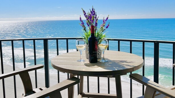 Un tavolo rotondo con due bicchieri da vino e una bottiglia, con vista sull'oceano e su un cielo sereno.