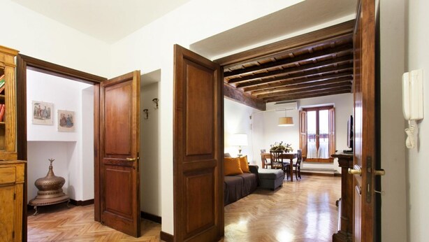 Un corridoio con pavimento in legno, una porta di legno e un'area pranzo con tavolo e sedie.