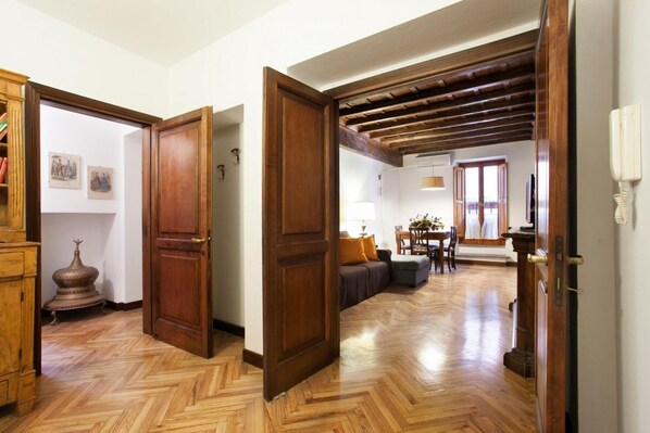 A hallway with wooden flooring, a wooden door, and a dining area with a table and chairs.