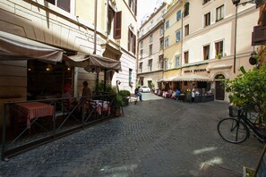 A cobblestone street with outdoor seating at a café, surrounded by buildings with balconies and awnings.