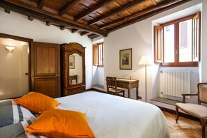 A bedroom with a large bed, wooden furniture, a desk, and a window with shutters.