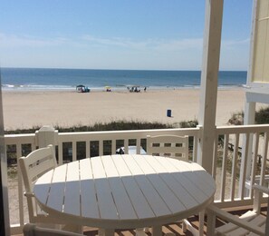 Blick auf einen Strand von einer überdachten Terrasse mit einem runden Tisch und Stühlen.