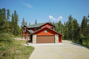 Stunning two-story home with a red exterior, set amidst lush greenery and a driveway.