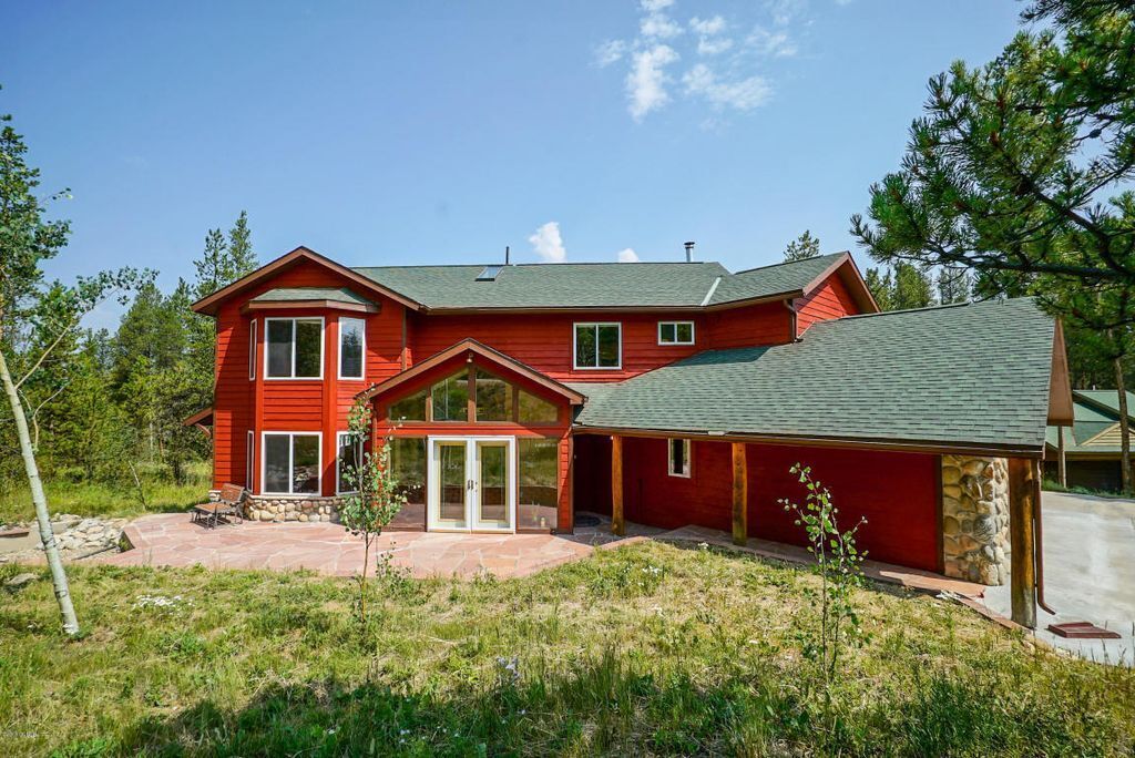 A red two-story house with a stone foundation, a covered patio, and a garage.