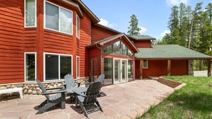 A red wooden house with a stone patio, outdoor seating, and a covered area. - Huge, Family Friendly, 6BR Retreat! Sleeps 16! All King Beds. Hot Tub and Sauna! (Winter Park)