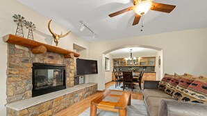 A cozy living room with a stone fireplace, a flat-screen TV, and a ceiling fan. - Huge, Family Friendly, 6BR Retreat! Sleeps 16! All King Beds. Hot Tub and Sauna! (Winter Park)