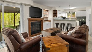 A modern living room with a fireplace, comfortable seating, a flat-screen TV, and a kitchen area with bar stools. - Huge, Family Friendly, 6BR Retreat! Sleeps 16! All King Beds. Hot Tub and Sauna! (Winter Park)