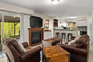 Cozy living area with fireplace, comfortable seating, and a TV. The kitchen area features a countertop and bar stools, with a sliding glass door leading to an outdoor space.