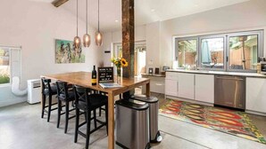 A modern kitchen with a wooden table, hanging pendant lights, and a stainless steel trash bin. - Frontside Hacienda downtown Salida. STR #012962 (Salida)