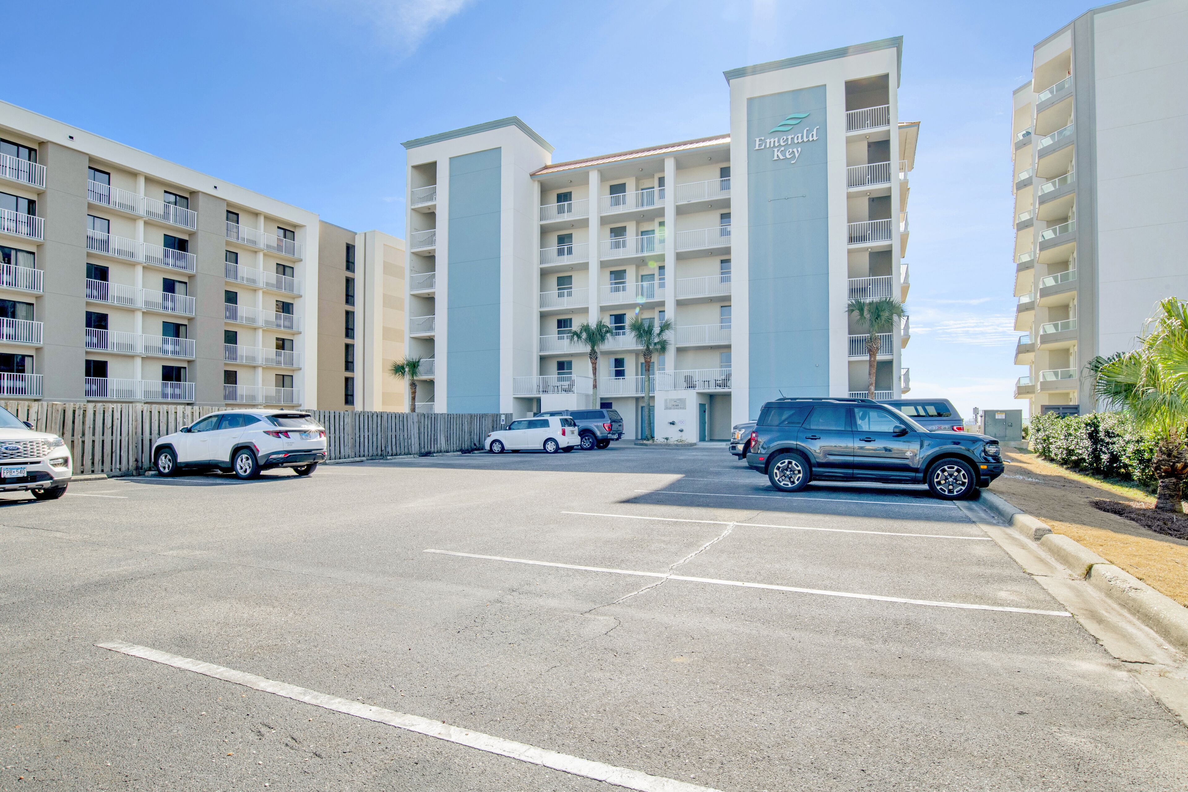 A multi-story hotel with balconies, a parking lot, and several parked cars.