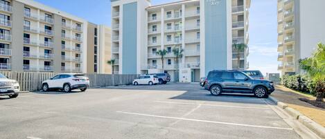 A multi-story hotel with balconies, a parking lot, and several parked cars.