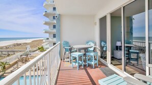 Un balcon avec vue sur la plage, une piscine et un espace repas avec des chaises et une table.