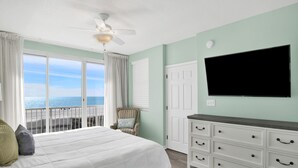 Une chambre avec un grand lit, un ventilateur de plafond, une télévision, une commode et une vue sur l’océan.