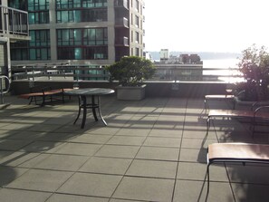 A rooftop terrace with a table and benches, overlooking a body of water and buildings.