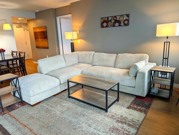A modern living room with a sectional sofa, a coffee table, and a dining area with chairs and a table.