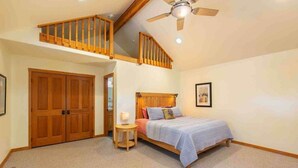A bedroom with a bed, wooden wardrobe, a small bedside table, a ceiling fan, and a staircase.