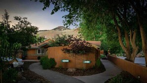 A building with a curved driveway leading to a gated entrance, surrounded by trees and a mountain in the background.