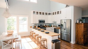 Una cocina moderna con armarios blancos, encimera de madera y electrodomésticos de acero inoxidable, además de un ventanal grande.