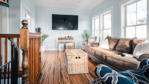 Una sala de estar con escalera de madera, un ventanal amplio, un sofá y un televisor de pantalla plana.