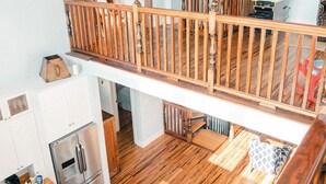 Una cocina amplia con piso de madera, un comedor con sillas, una escalera de madera y una tabla de surf al fondo.