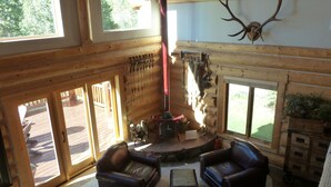 Interior de cabana de madeira com sofás de couro, lareira e cabeça de veado montada.