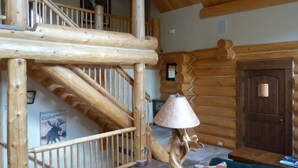 Interior de uma cabana de madeira com escada, abajur e sofá.