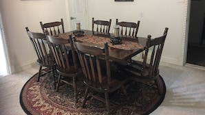 Comedor con una mesa redonda, seis sillas de madera, un camino de mesa estampado y dos cuadros colgados en la pared.