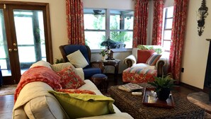 A cozy living room with a sofa, armchairs, and a coffee table. There is a window with curtains, a door, and a small table with a plant. - A SLICE OF "OLD FLORIDA" AMONG GRANDFATHER OAKS. (Crystal River)