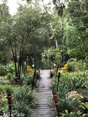 A wooden pathway leading through a lush garden with various plants and trees. - A SLICE OF "OLD FLORIDA" AMONG GRANDFATHER OAKS. (Crystal River)