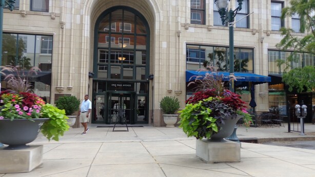 A building with a large arched entrance, outdoor seating, and potted plants.